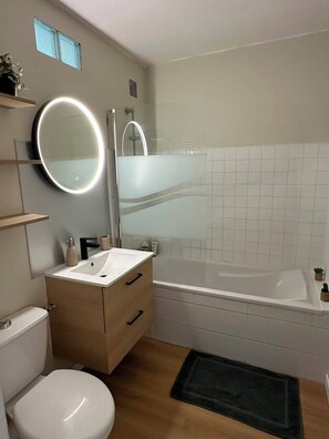 Een moderne badkamer met toilet, wastafel, spiegel, douche en bad.