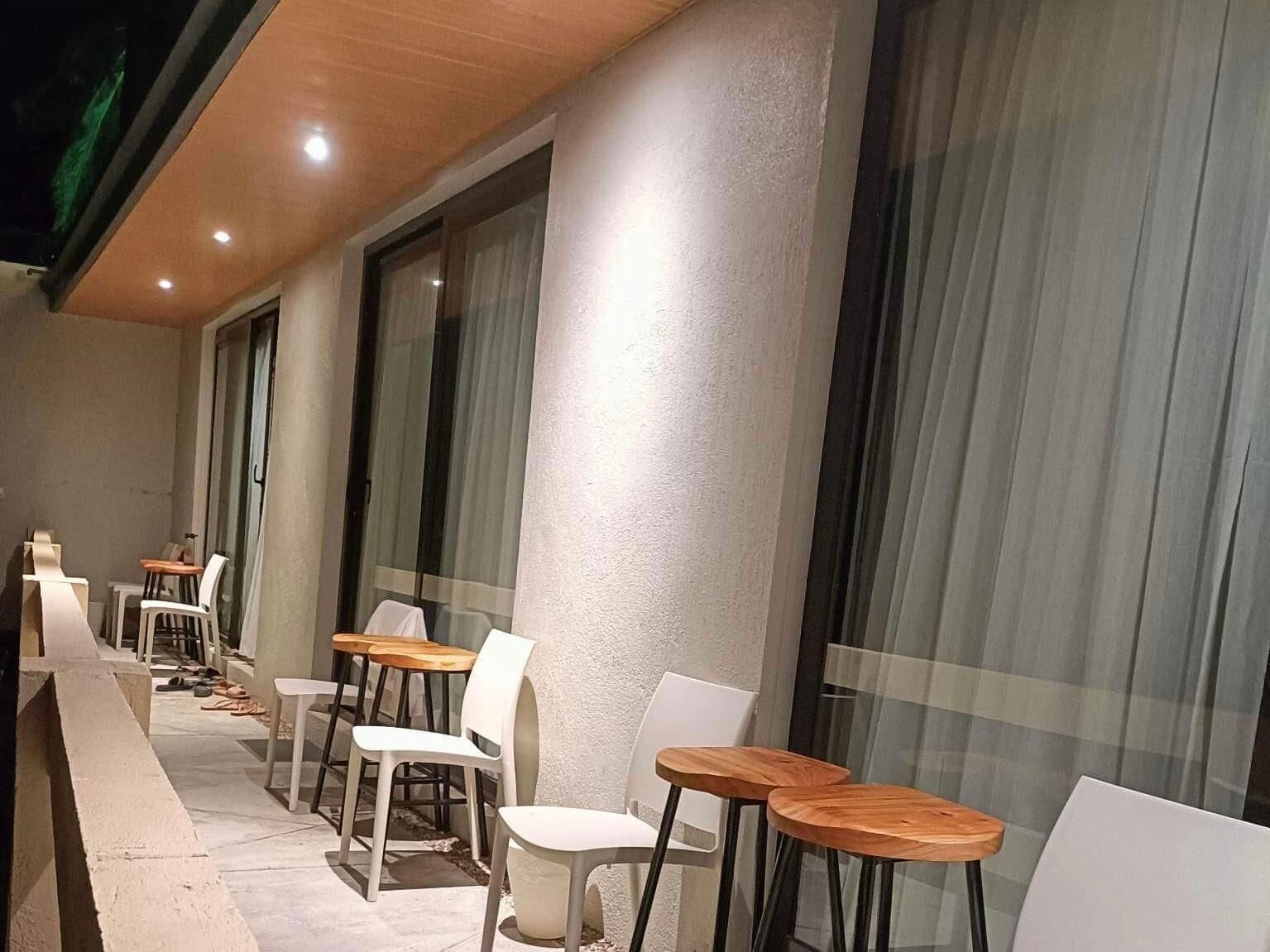 A covered outdoor seating area with tables and chairs, large windows, and a ceiling with recessed lighting.