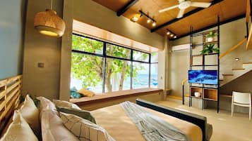 A bedroom with a large bed, a TV, a window with a view of the sea, and a staircase.