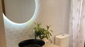 A bathroom with a round mirror, a sink with a copper basin, a potted plant, a toilet, and a shower curtain with a leaf pattern. - Marzon Beach Resort (MANOC MALAY AKLAN)