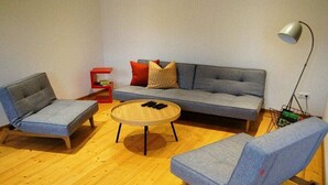 Ein Wohnzimmer mit grauem Sofa, zwei grauen Sesseln, einem runden Couchtisch und einem roten Beistelltisch.