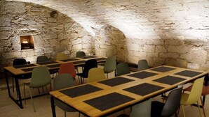 Ein Zimmer mit Steinwänden, Tischen mit schwarzen Unterlagen und bunten Stühlen.