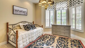 Une chambre à coucher avec un lit, une commode, un lustre et une fenêtre avec des volets.
