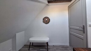 A small, enclosed room with a white bench, a wooden door, and a wall-mounted decorative item.