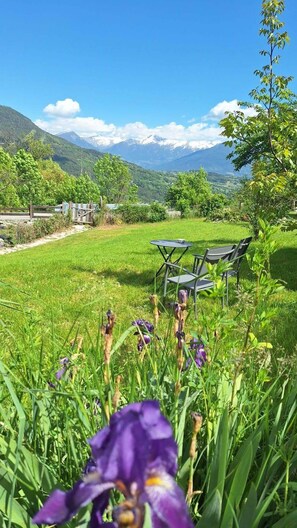 A grassy outdoor area with a table and chairs, surrounded by mountains and a clear sky. - Garden house with stunning mountain views near the lake – Aux Rousses, Réallon (Réallon)