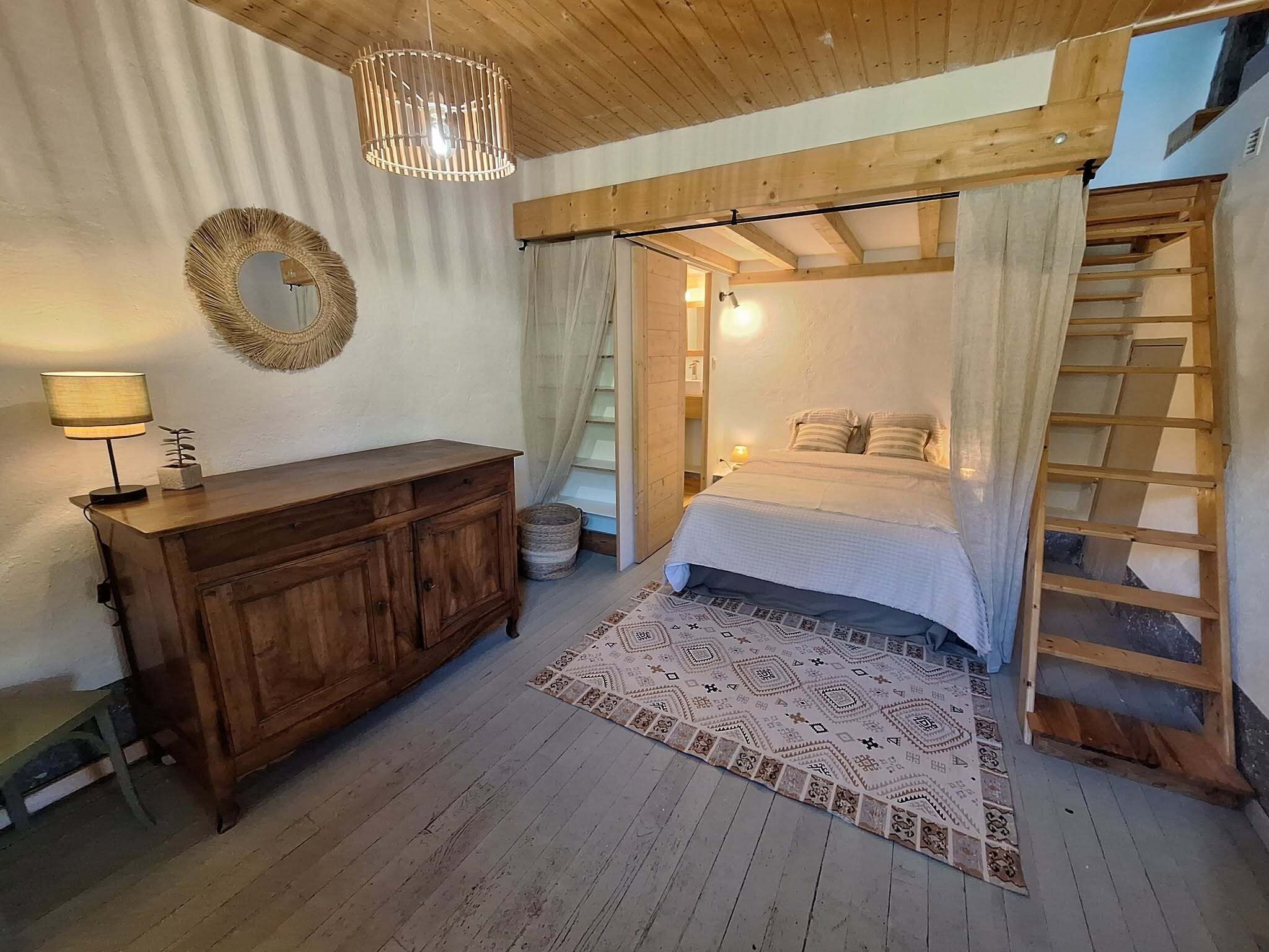 Une chambre à coucher avec un lit en bois, une table de chevet, une lampe, un miroir et une échelle.