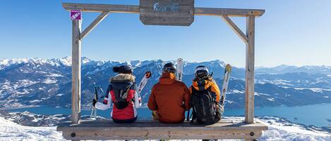 A wooden bench with a sign reading 'Réallon' in a snowy landscape with mountains and a lake in the background.