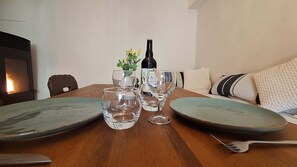 A dining table set with plates, glasses, and a bottle, with a sofa and pillows in the background.