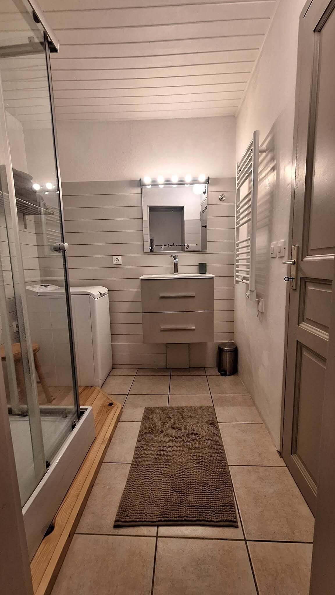 Ein kompaktes Badezimmer mit Glasdusche, Waschtisch mit Spiegel und einem kleinen Teppich.