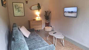 A living room with a grey sofa, a small round table, a wooden cabinet, a mirror, and a framed picture on the wall.