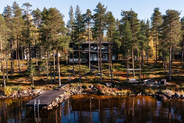 A cabin surrounded by a forest with a dock extending into a lake.