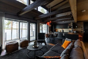 A modern interior with a dining area, kitchen, and large windows overlooking a body of water. - Willa Lumia - Aurora Skylight Villa (Rovaniemi)