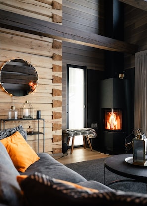 Een gezellige woonkamer met een open haard, een ronde spiegel en een bank met kussens.