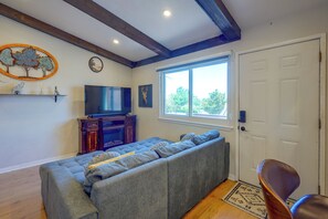 Una sala de estar con un sofá modular, un televisor, una planta decorativa y una ventana con vistas a árboles.