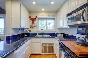 Una cocina con armarios blancos, lavavajillas de acero inoxidable, microondas y hervidor sobre una encimera de madera.