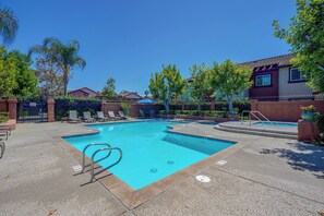 Una piscina rectangular con borde azul, rodeada de sillones de descanso y una terraza pavimentada.
