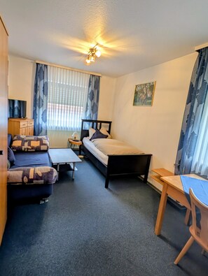 A compact hotel room with a bed, a sofa, a small table, and a desk.