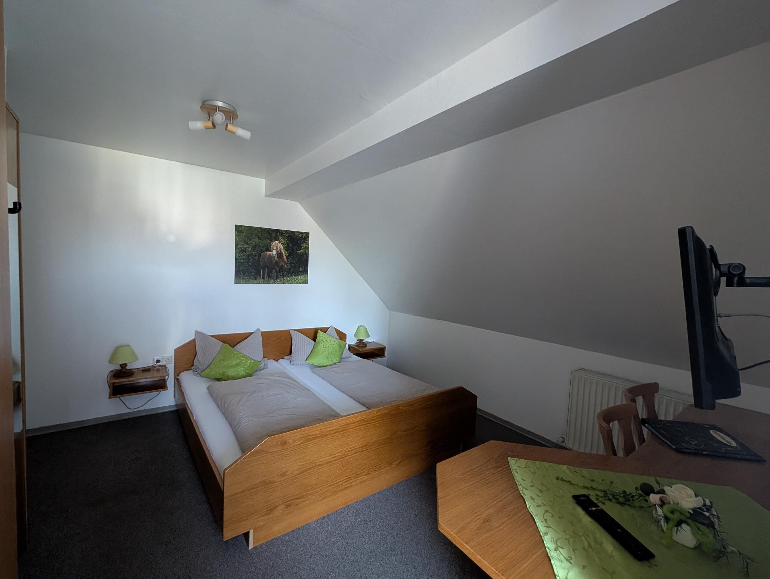 Ein Schlafzimmer mit einem Bett, Nachttischen, einem Schreibtisch, einem Sessel, einer Lampe, einem Bild an der Wand und einem Deckenventilator.