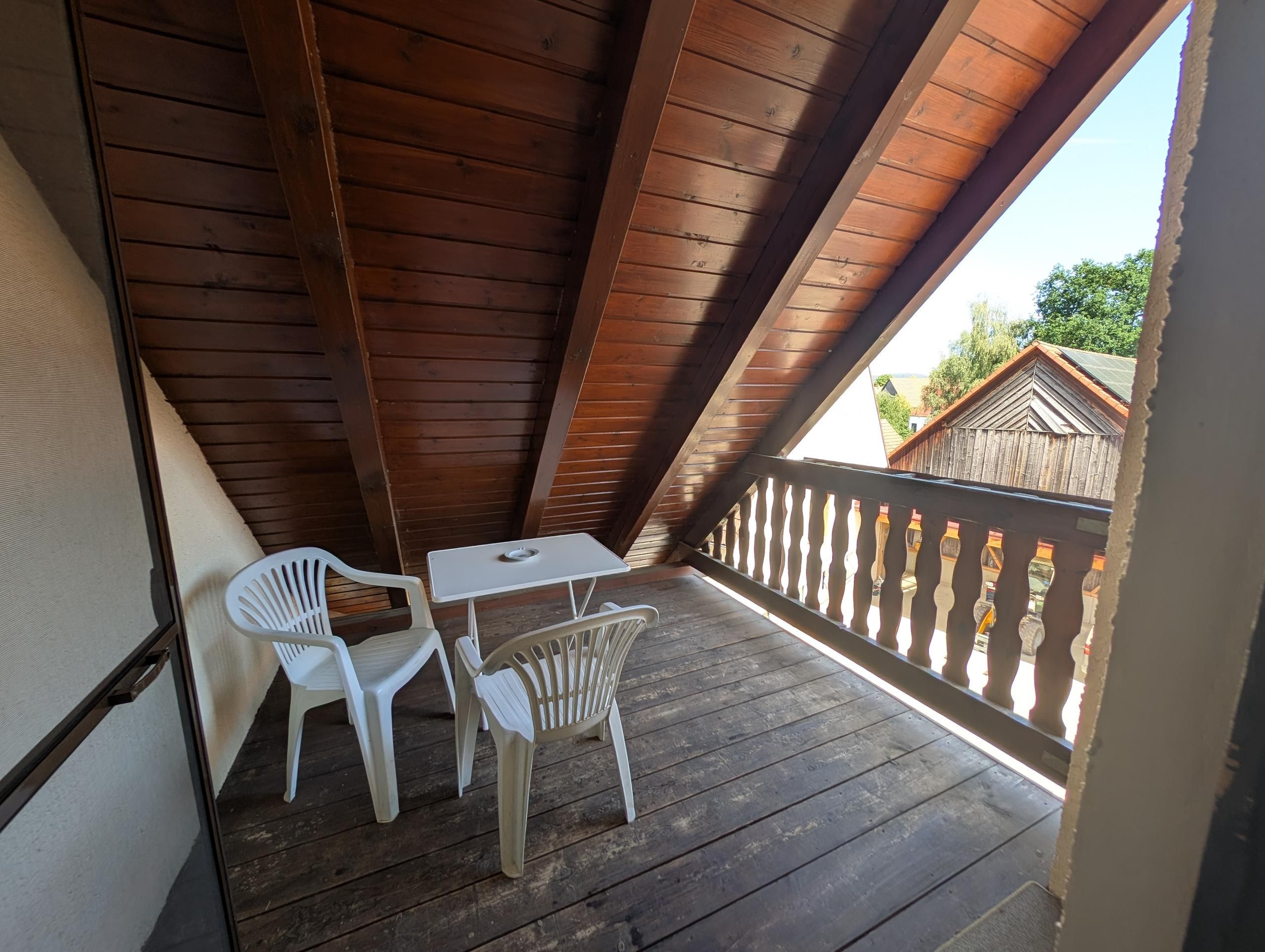Un balcón de madera con una mesa y dos sillas, con vistas a una zona residencial.