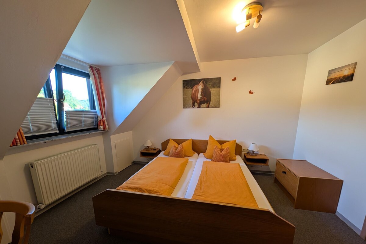 A bedroom with a large bed, a radiator, a window with curtains, and a ceiling light fixture.