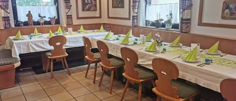 Comedor con mesas dispuestas para varios comensales, sillas y lámparas colgantes.
