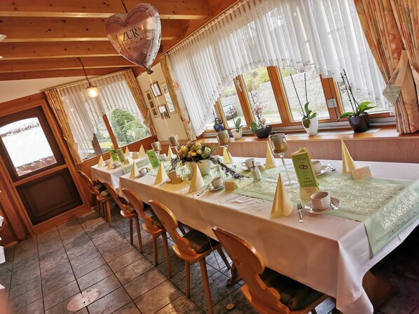 A long dining table set with white tablecloths, gold napkins, and a heart-shaped balloon.