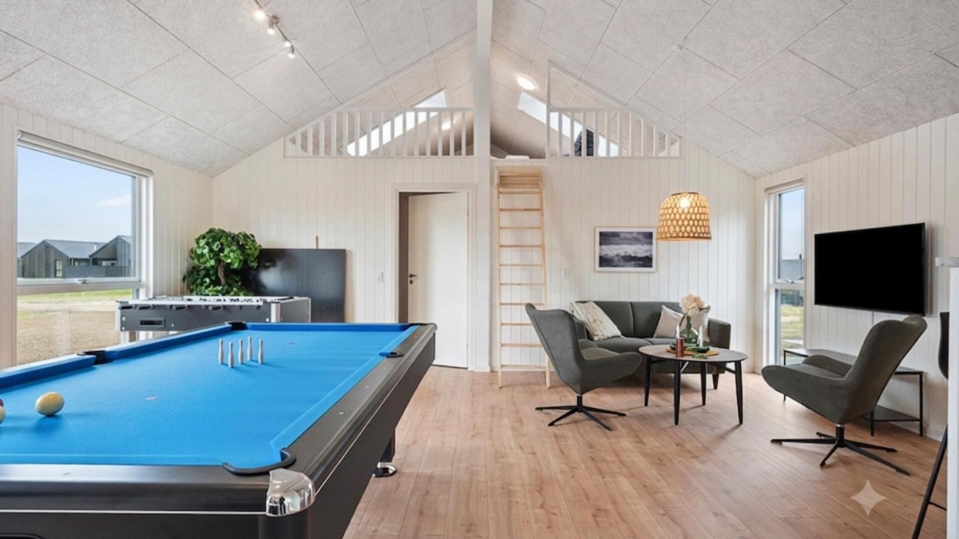 Ein modernes Wohnzimmer mit Billardtisch, einer Couch, einem Fernseher und Blick ins Freie.