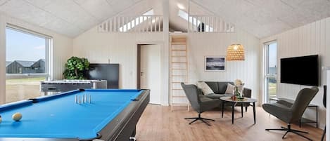 A modern living room with a pool table, a sofa, a TV, and a view of the outside.