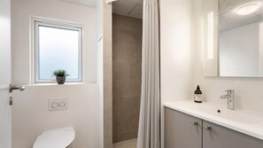 Ein Badezimmer mit Toilette, einem Fenster mit Pflanze, einer Duschkabine und einem Waschbecken mit Spiegel.