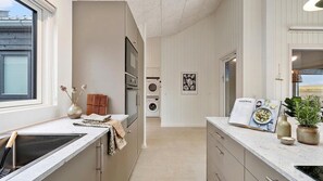 A modern kitchen with a built-in oven, a washing machine, and a dining area with a cookbook. - VillaVilla 957 - Skåstrup Strand, Fyn og øer (Bogense)