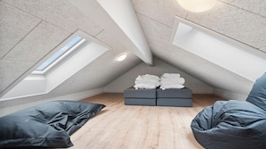 Ein Schlafzimmer im Loft-Stil mit schrägem Dach, einem Oberlicht, einem Bett und einer Sitzecke mit Kissen.