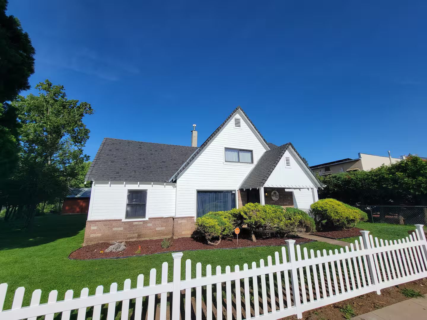 A single-story house with a gabled roof, a front porch, and a white picket fence.