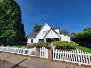 Une maison de plain-pied à l’extérieur blanc, avec des fondations en briques et une clôture en bois peinte en blanc.