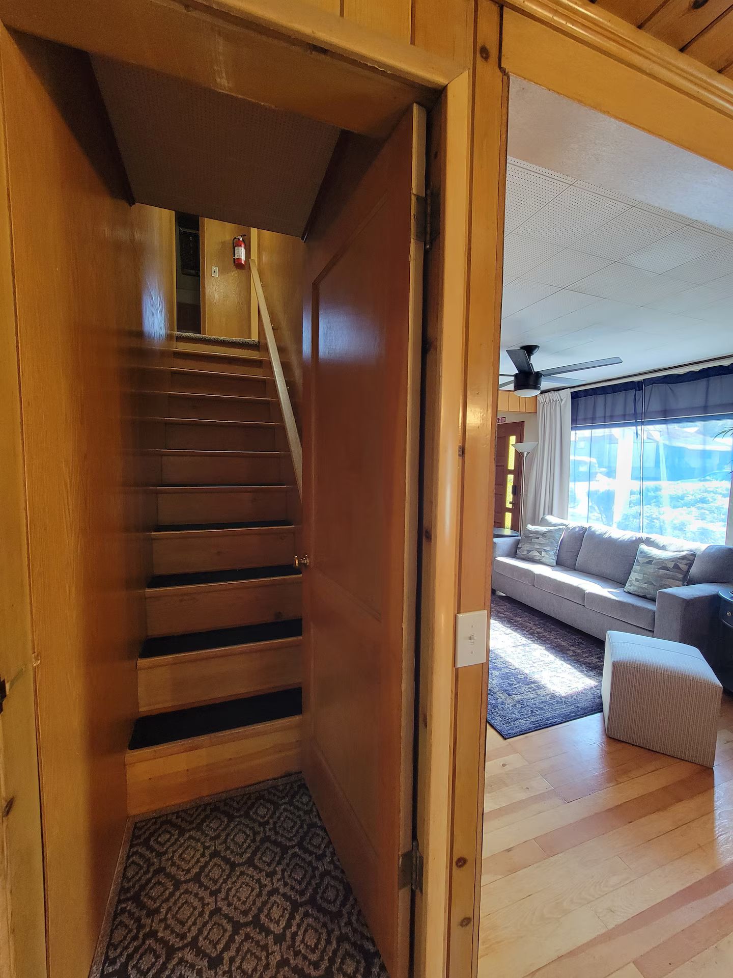 Una escalera de madera que lleva a una habitación con un sofá y una alfombra estampada.