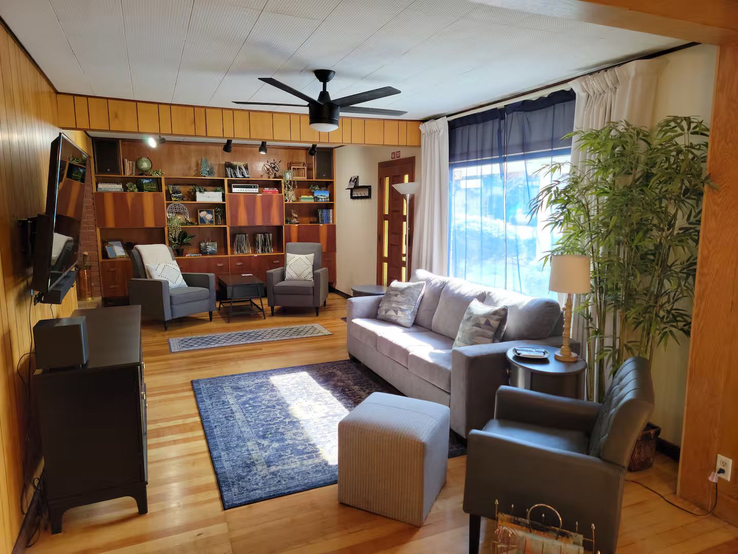 A living room with a sofa, armchairs, a coffee table, a TV, a bookshelf, and a ceiling fan.