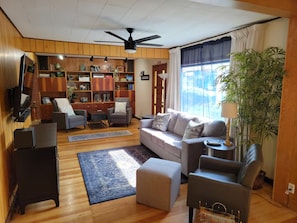 Un salon comprenant un canapé, des fauteuils, une table basse, un téléviseur, une bibliothèque et un ventilateur de plafond.