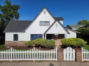 A white single-story house with a gabled roof, a front porch, and a white picket fence.