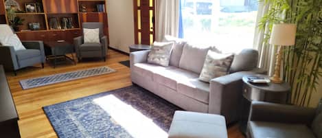 A living room with a sofa, armchairs, a coffee table, a bookshelf, and a large window with a view.