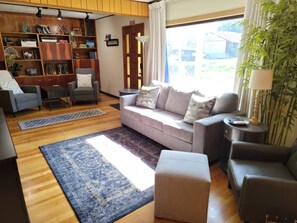 Un salon comprenant un canapé, des fauteuils, une table basse, une bibliothèque et une grande fenêtre donnant sur un beau paysage.