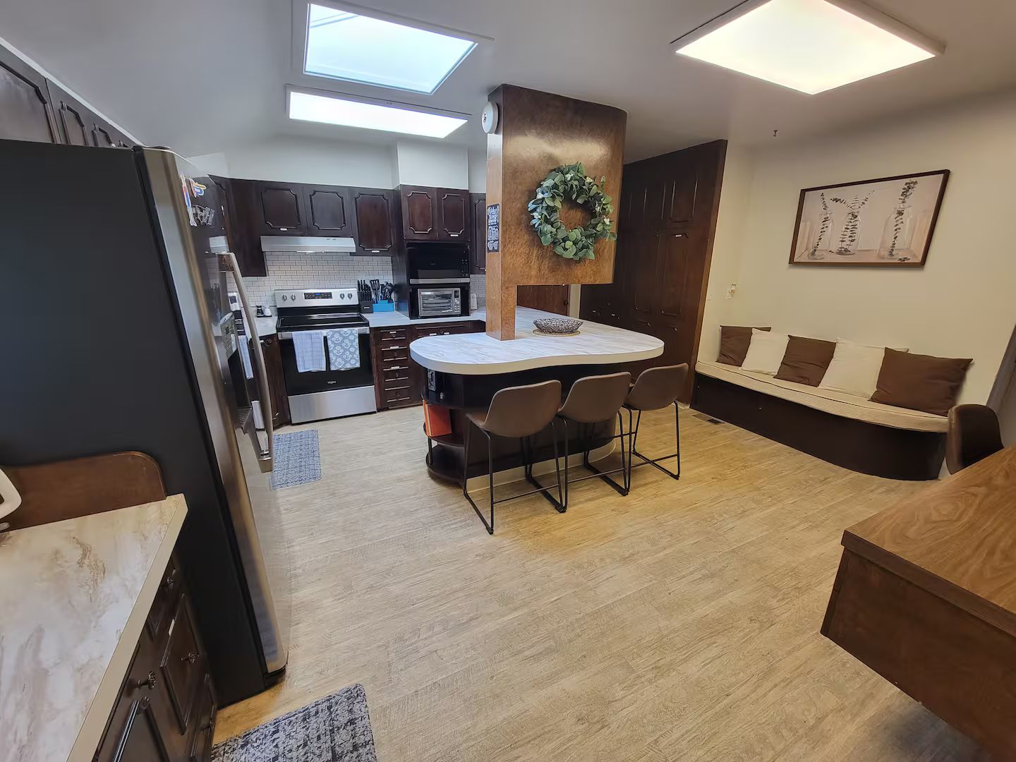 A compact kitchen with a central island, a dining area with a sofa, and a view of the outside.