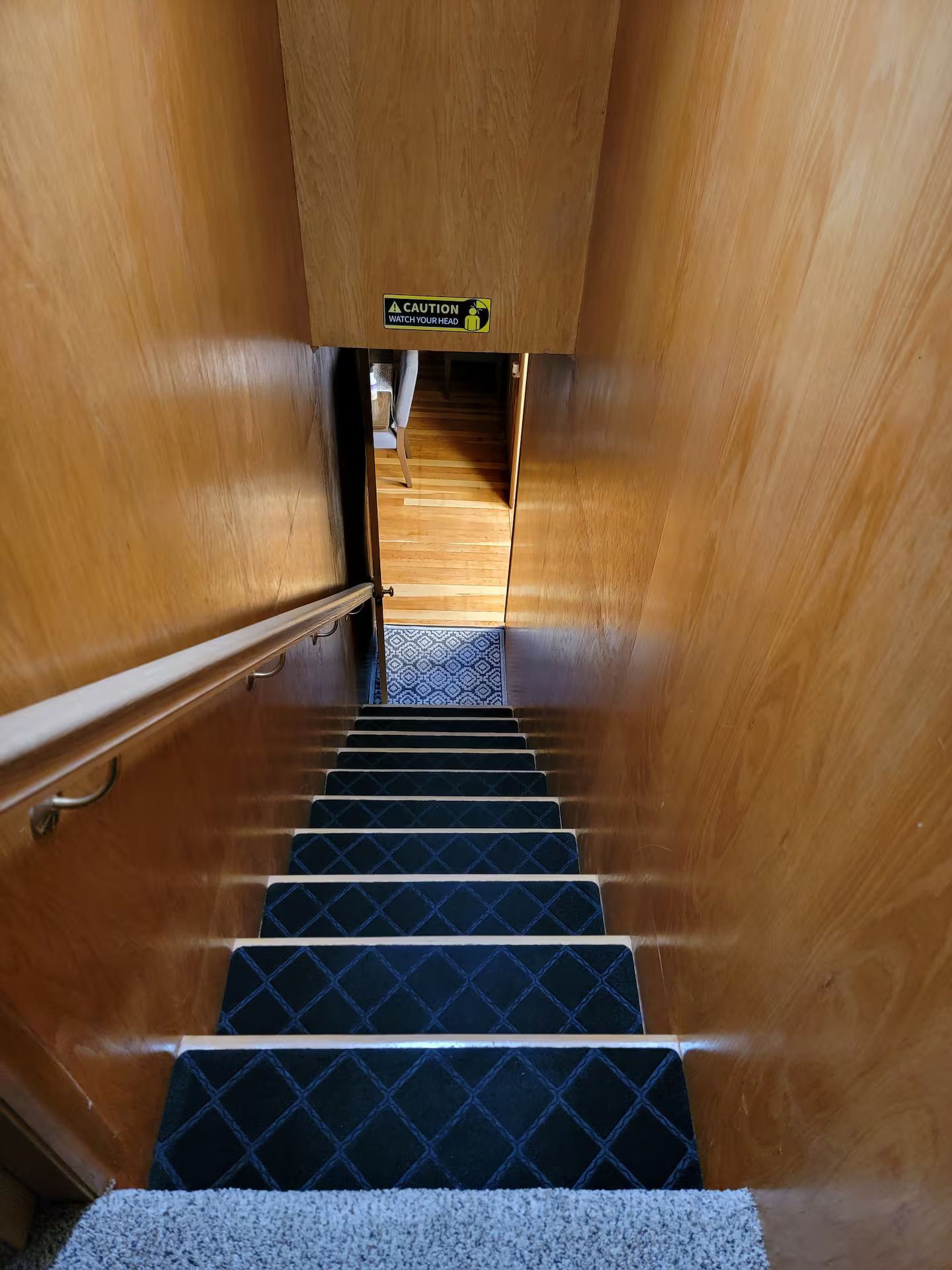 Een houten trap met een waarschuwingsbord, leidend naar een kamer met een kamerbreed tapijt.