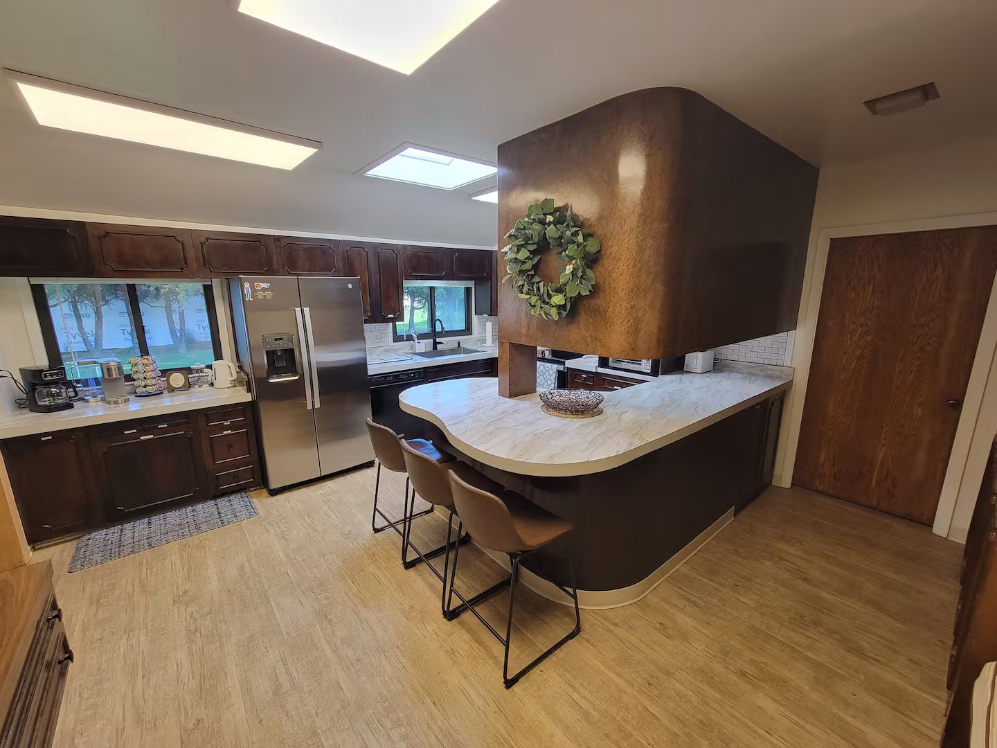 A modern kitchen with a curved island, stainless steel appliances, and a large window.