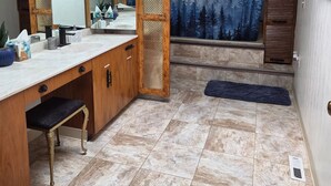 A bathroom with a wooden vanity, a large mirror, a shower curtain with a forest design, and a skylight. - Carlton Cottage (Burney)