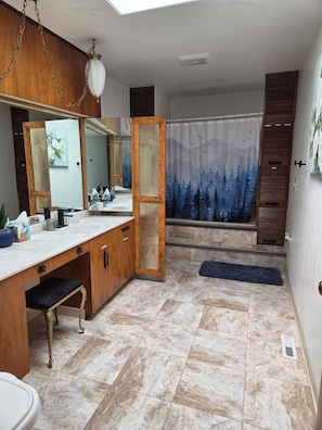 Une salle de bain avec un meuble-lavabo en bois, un grand miroir, un rideau de douche orné d’un motif de forêt et une lucarne.