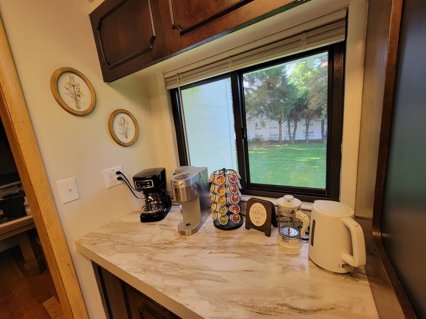 A kitchen counter with a coffee maker, a kettle, a mug, and a coffee pod holder.