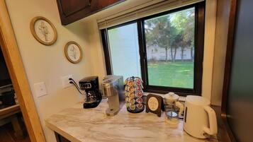 A kitchen counter with a coffee maker, a kettle, a mug, and a coffee pod holder.