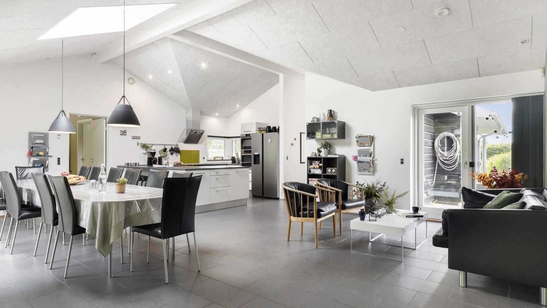 A spacious living area with a dining table, chairs, and a sofa. There is a kitchen in the background with modern appliances.