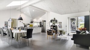 Un'ampia zona giorno con tavolo da pranzo, sedie e divano. Si nota una cucina sullo sfondo, dotata di elettrodomestici moderni.