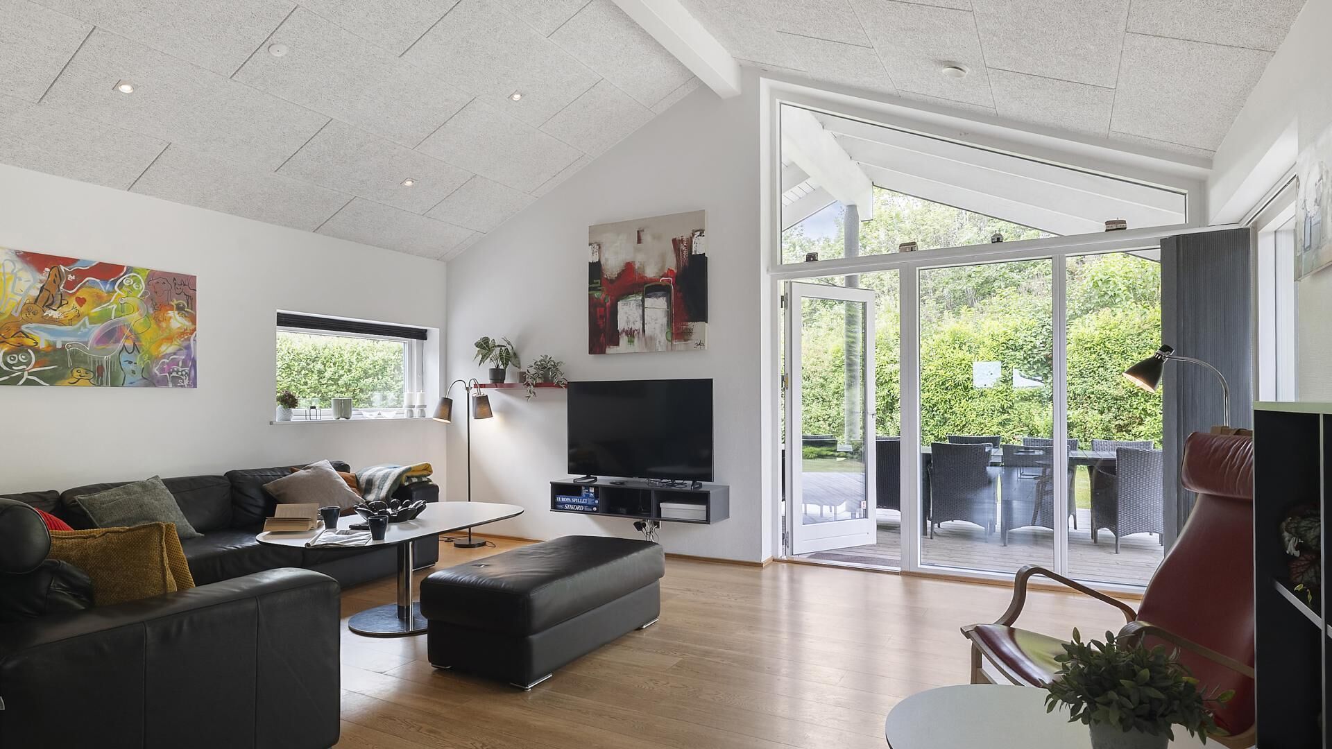 A modern living room with a flat-screen TV, a sofa, a coffee table, and a large window offering a view of the outdoors.