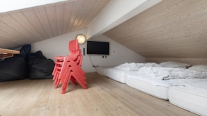 Ein Schlafzimmer im Loft-Stil mit schrägem Dach, einem Bett, einem roten Sessel, einem Fernseher und einem Schreibtisch mit Lampe.